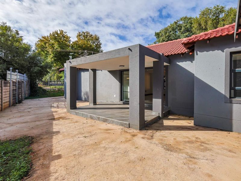 A rear view of the property featuring a covered patio area with tiled flooring and a large backyard space.