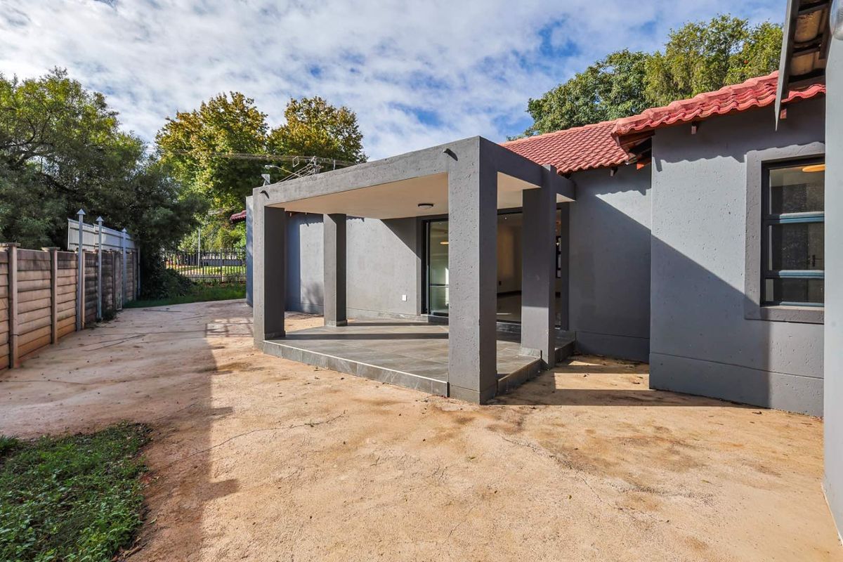 A rear view of the property featuring a covered patio area with tiled flooring and a large backyard space.