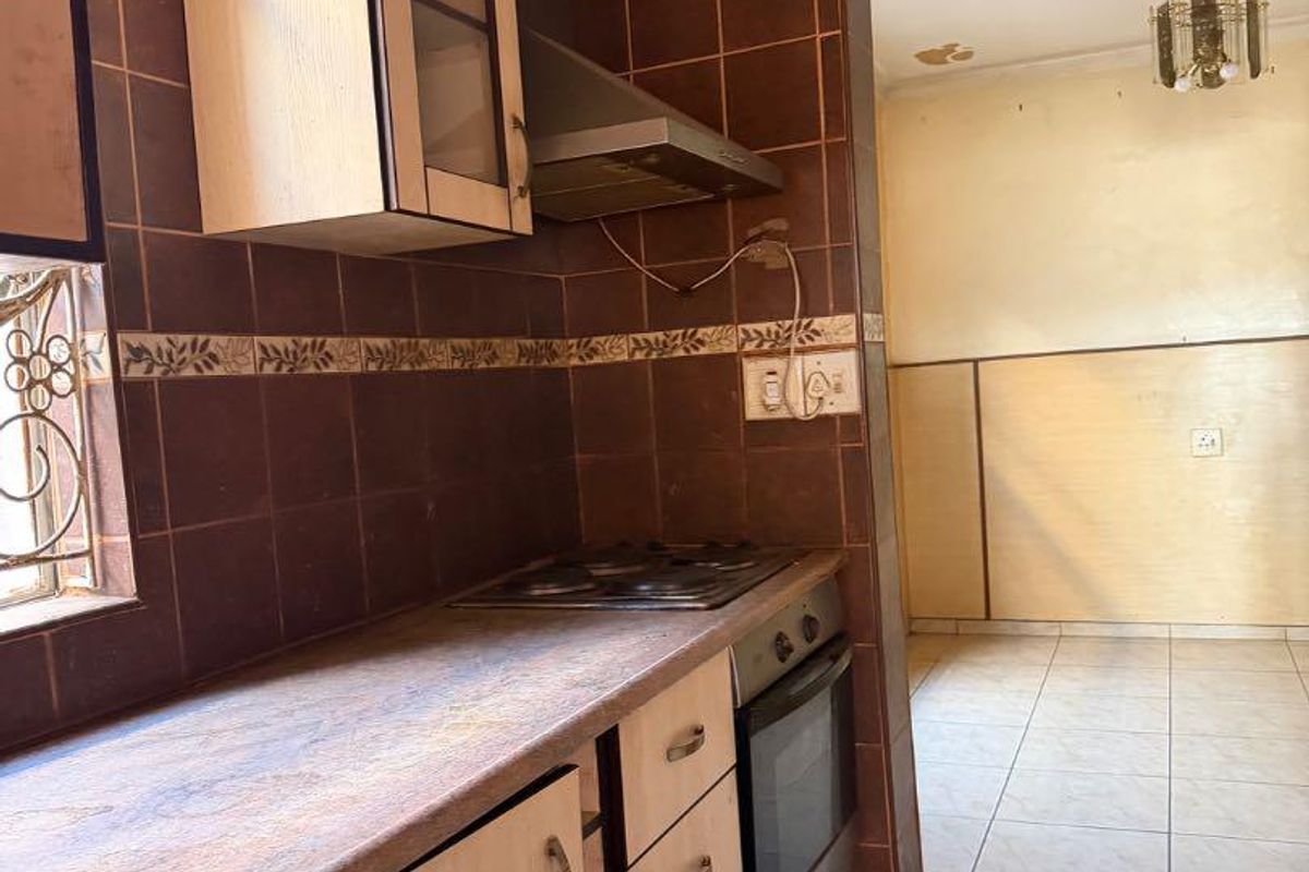 A functional kitchen featuring built-in cabinetry, a laminate countertop, an integrated oven and hob, and a tiled backsplash, leading into an adjacent living area.