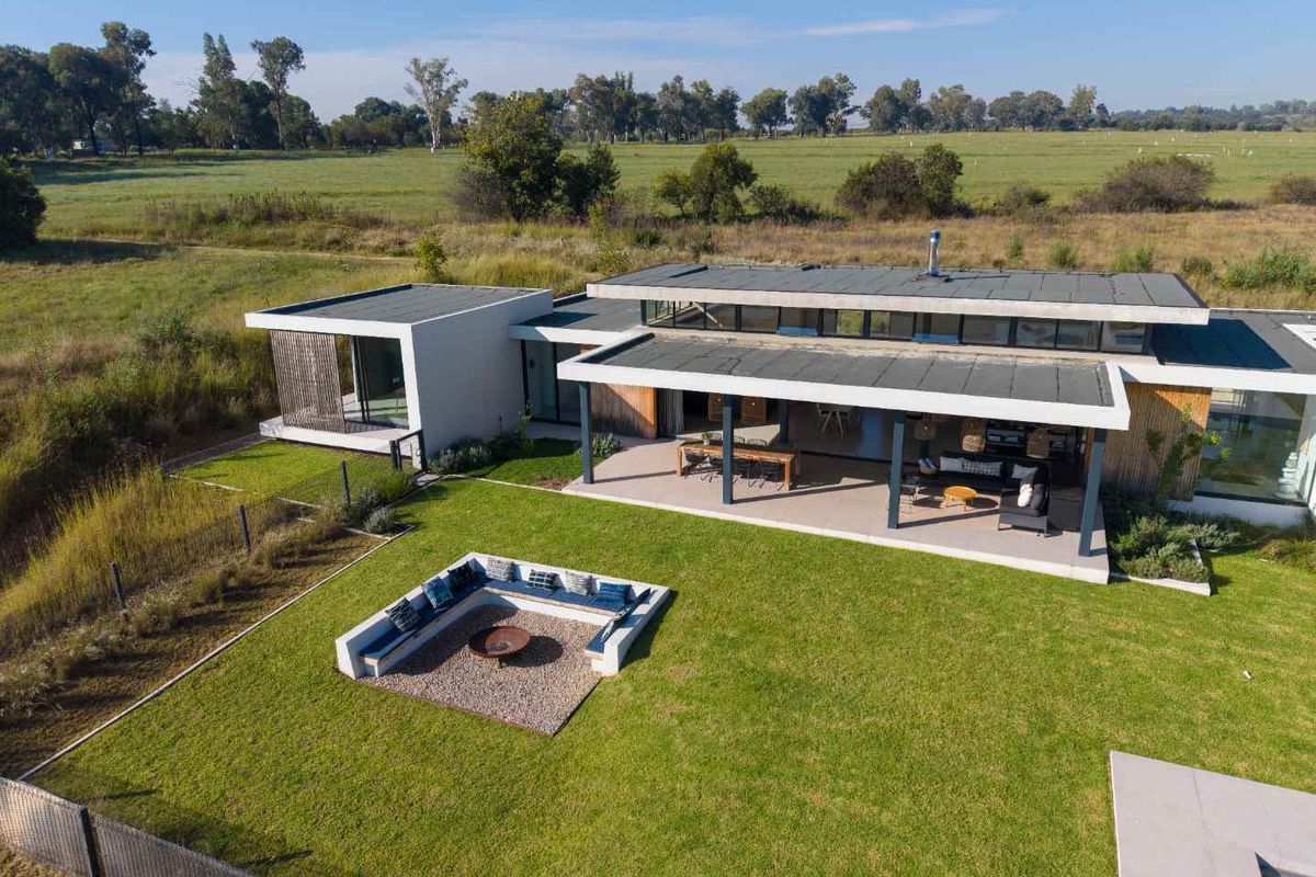 Aerial view of a modern single-story residence featuring a flat roof, covered patio, and a sunken fire pit area set within a landscaped garden.