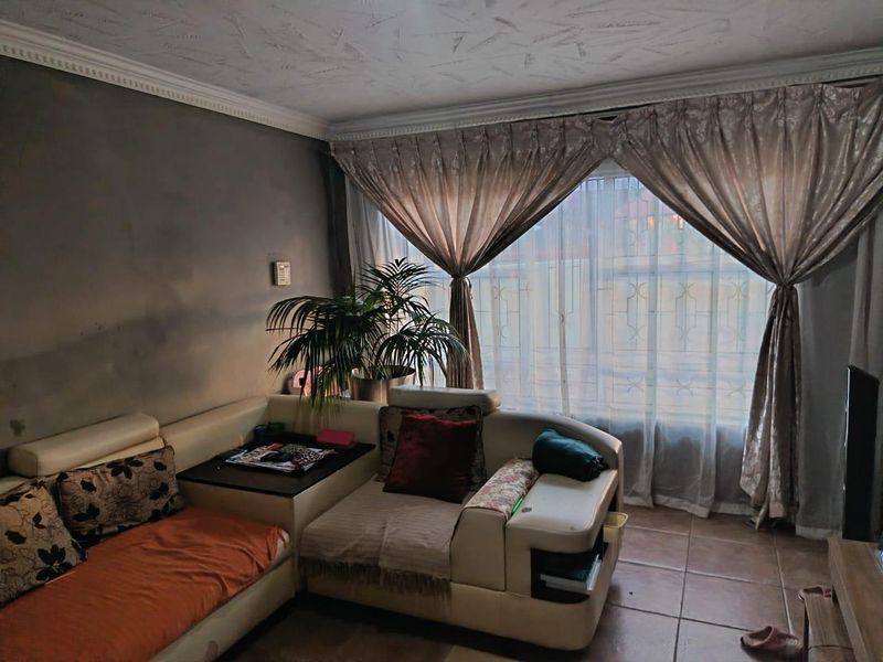 A living room featuring tiled flooring, textured ceilings with decorative cornicing, and large windows fitted with security bars.