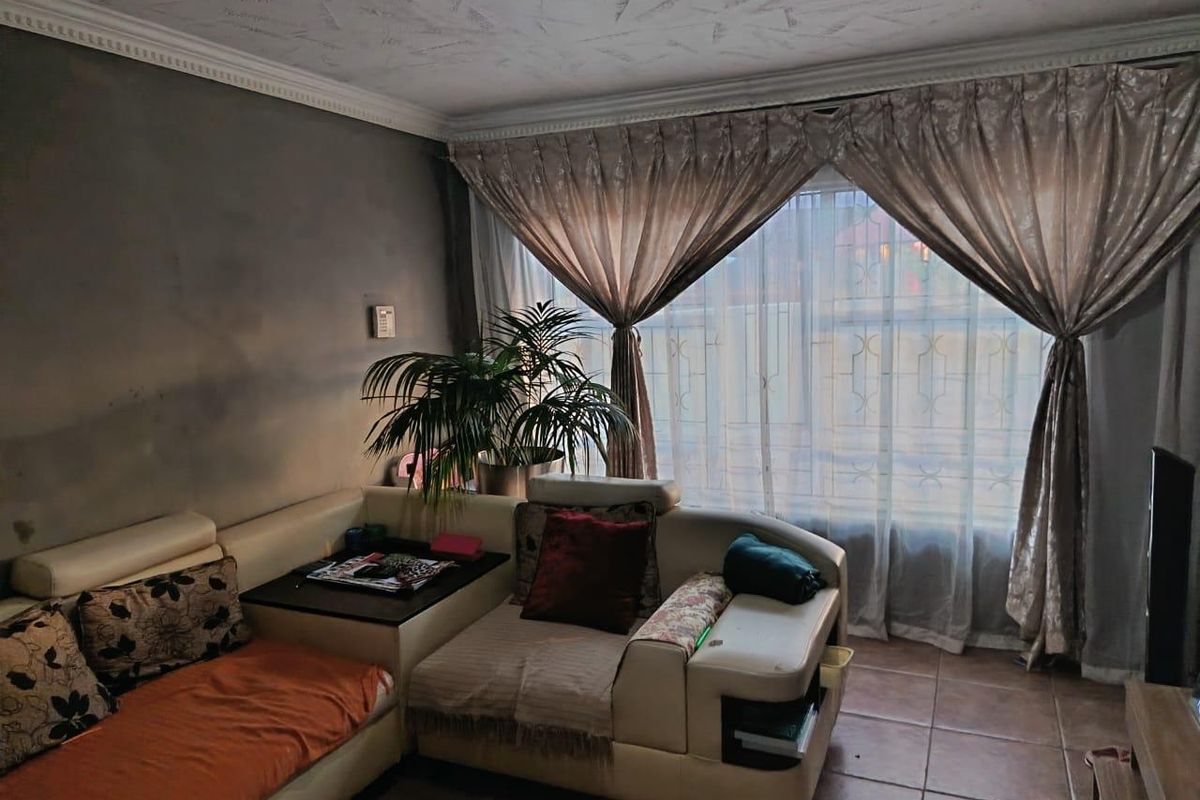 A living room featuring tiled flooring, textured ceilings with decorative cornicing, and large windows fitted with security bars.
