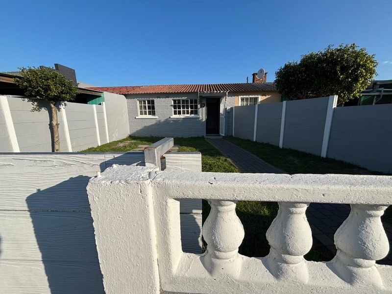 Front view of a single-story house featuring a brick facade, tiled roof, paved walkway, and a precast concrete boundary wall with a balustrade.