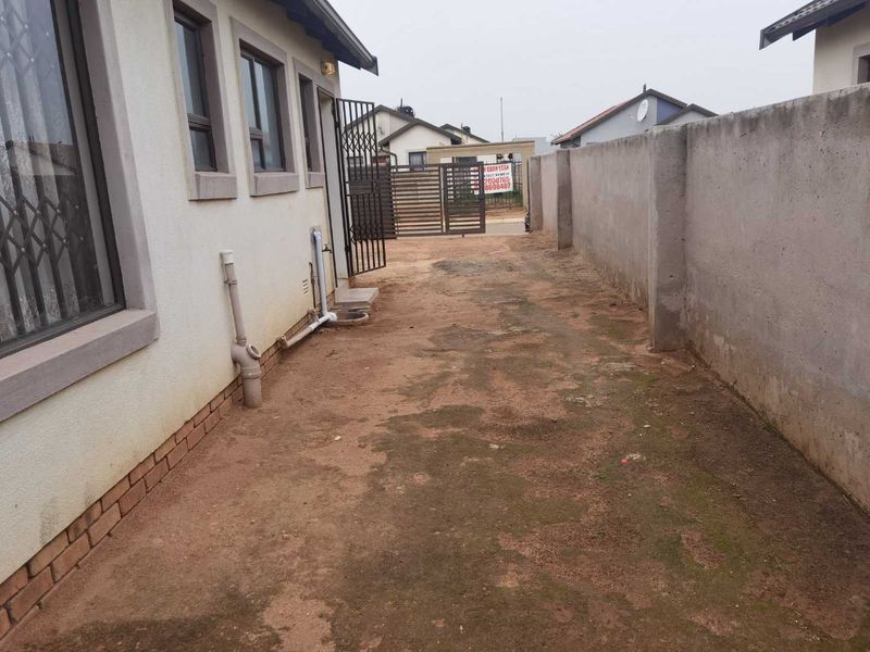 A side yard area featuring a perimeter wall, security gate, and exposed exterior plumbing along the side of the house.