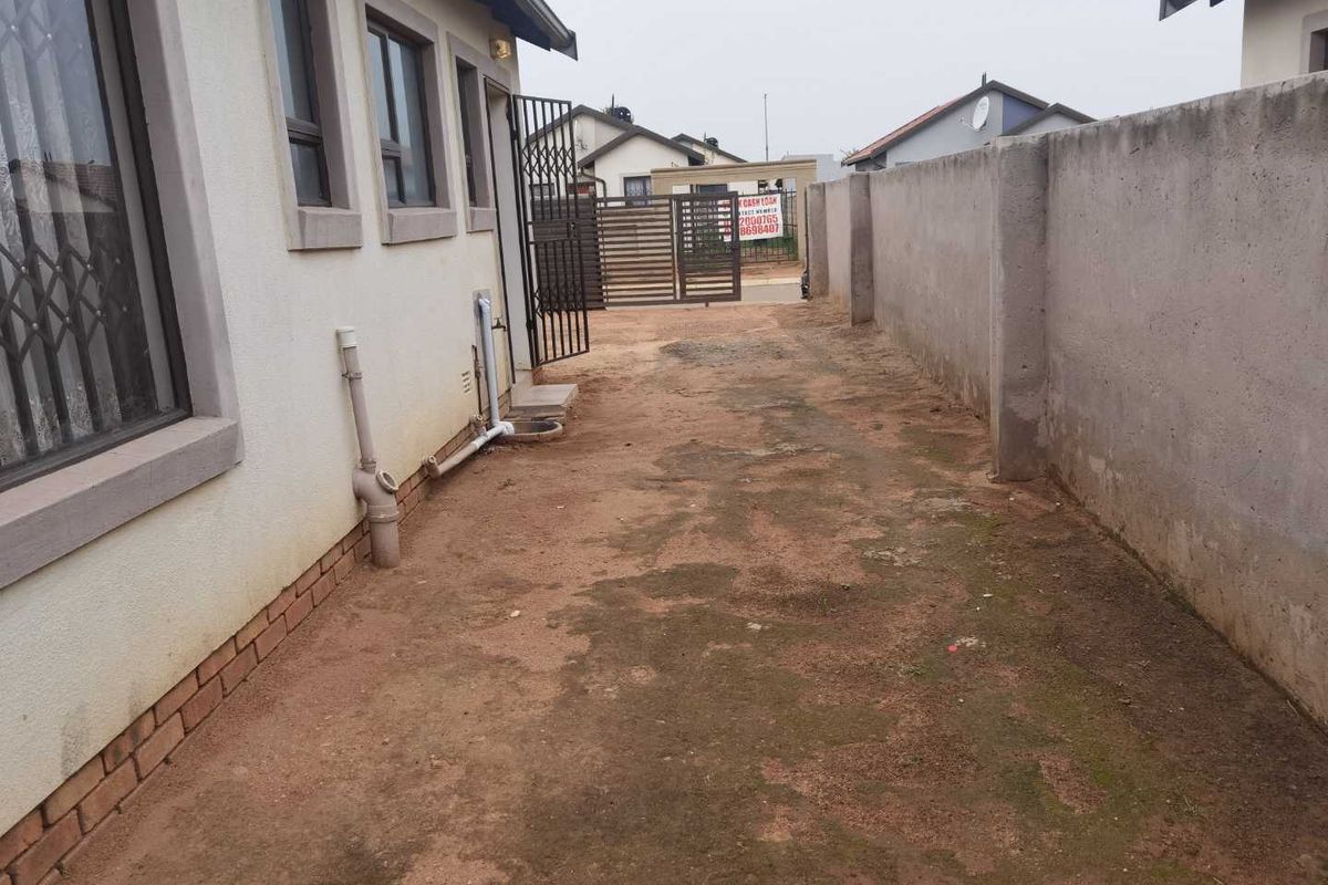 A side yard area featuring a perimeter wall, security gate, and exposed exterior plumbing along the side of the house.