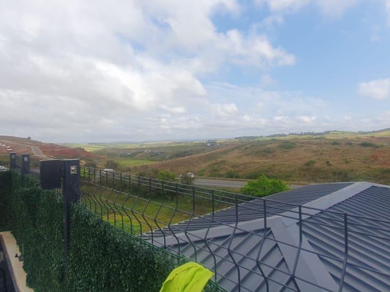 Elevated view overlooking rolling hills and landscape, featuring secure metal fencing and artificial hedge screening on the balcony perimeter.