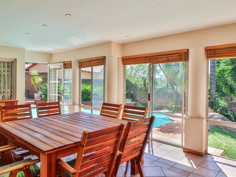 A bright, enclosed patio area featuring tiled flooring, recessed lighting, and multiple sliding glass doors providing direct access to the pool and garden area.