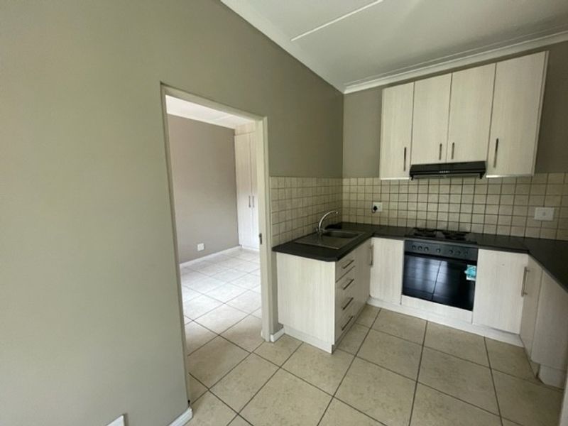 A functional kitchen featuring light-toned built-in cabinetry, tiled backsplash, integrated oven and hob, and tiled flooring, with an adjacent room visible.