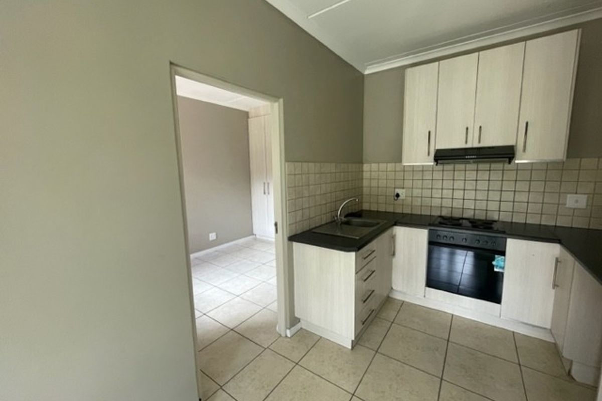 A functional kitchen featuring light-toned built-in cabinetry, tiled backsplash, integrated oven and hob, and tiled flooring, with an adjacent room visible.