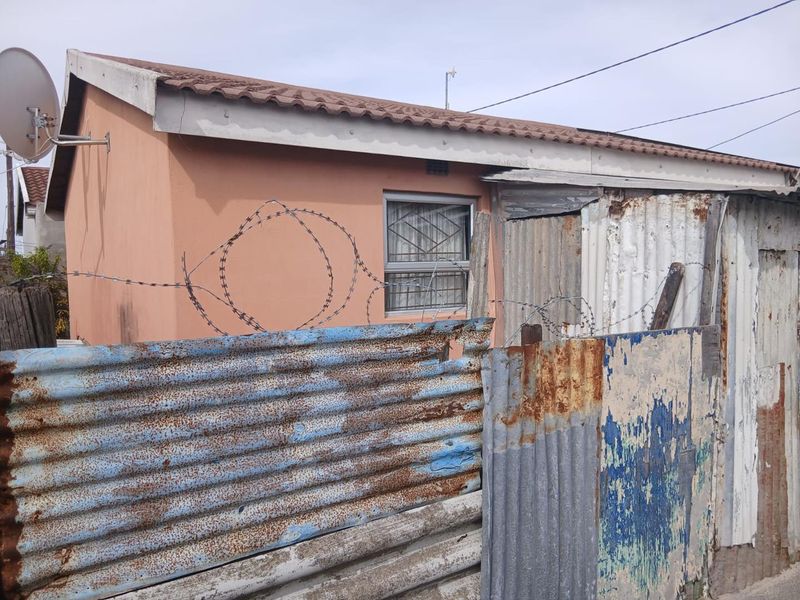 Exterior view of a residential property featuring a tiled roof, security bars on windows, and corrugated metal perimeter fencing with razor wire.