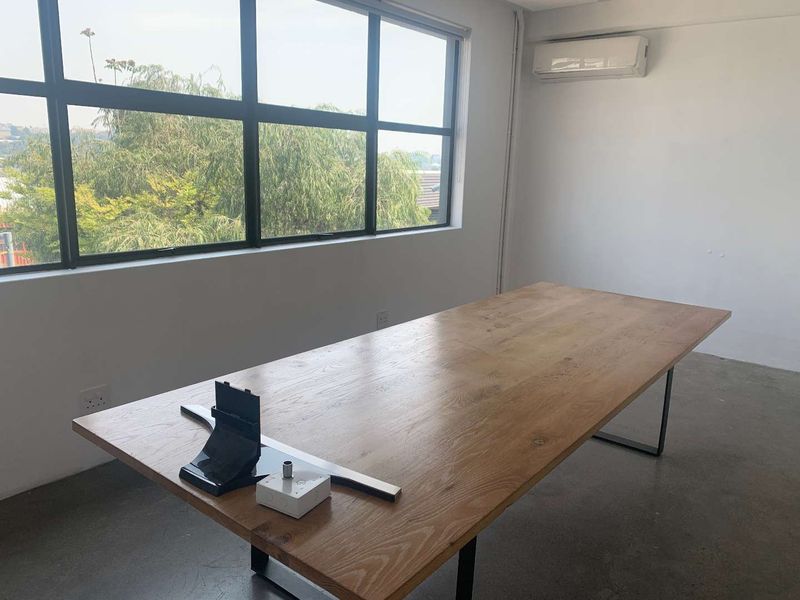 A bright office space featuring polished concrete floors, a large industrial-style window with natural light, and a wall-mounted air conditioning unit.