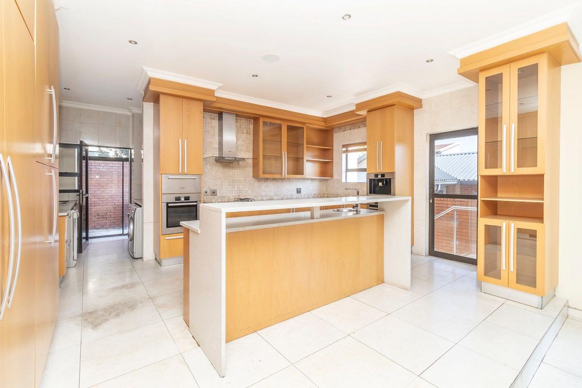 Spacious kitchen featuring light wood cabinetry, stone countertops, a breakfast bar, and integrated appliances, with direct access to an adjacent laundry area.