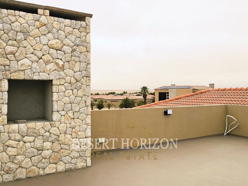An open-air rooftop balcony featuring a stone-clad built-in fireplace and views over the surrounding residential estate.