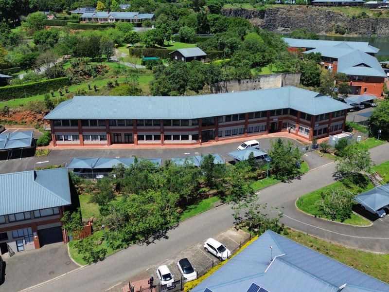Aerial view of a multi-story office complex featuring brick construction, metal roofing, and extensive covered parking facilities within a landscaped estate setting.