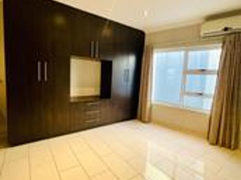A spacious bedroom featuring large dark wood built-in cupboards, polished tiled flooring, recessed lighting, and a wall-mounted air conditioning unit.