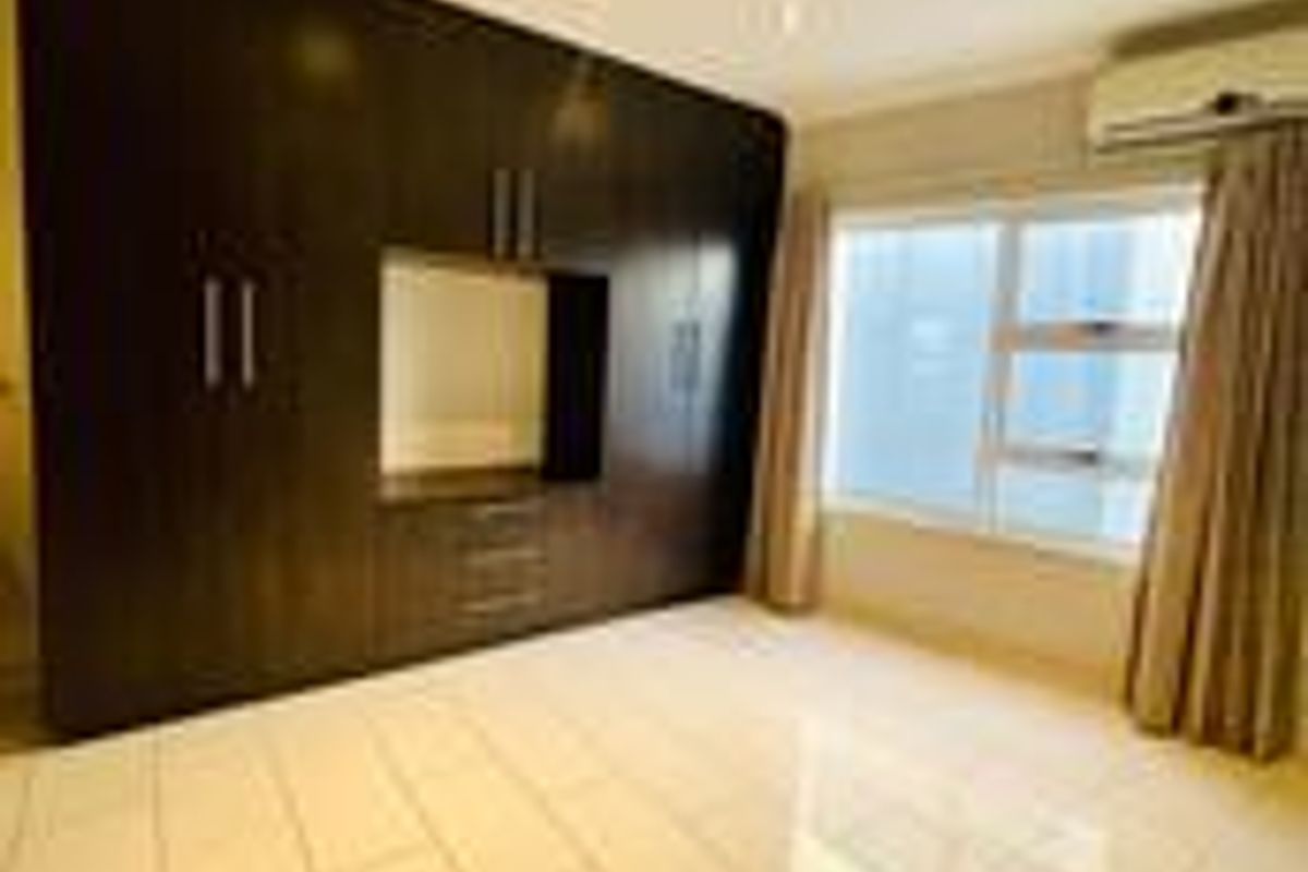 A spacious bedroom featuring large dark wood built-in cupboards, polished tiled flooring, recessed lighting, and a wall-mounted air conditioning unit.