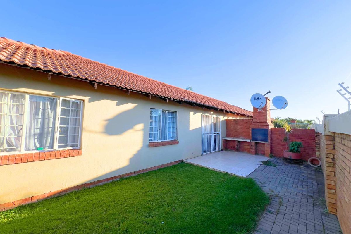 Rear view of the townhouse featuring a paved patio area, built-in brick braai, and a small private garden space.