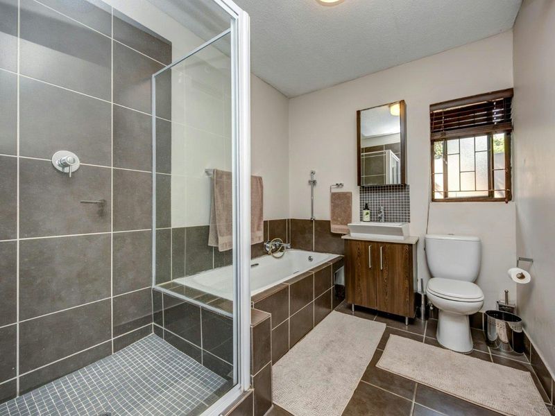 A well-maintained bathroom featuring a glass-enclosed shower, a built-in bathtub, a vanity cabinet with a basin, and a toilet.