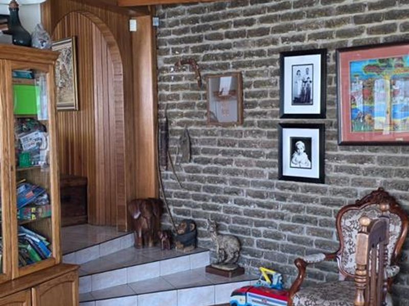 Living area featuring exposed timber ceiling beams, a rustic brick feature wall, and an arched doorway leading to a raised tiled section.