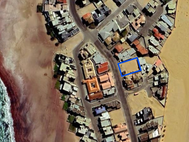 An aerial view showing a vacant residential land plot situated in a coastal neighborhood near the beach.