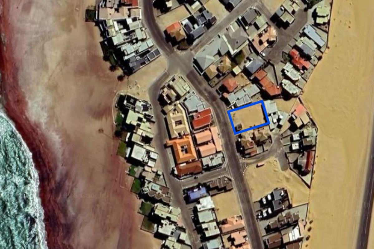 An aerial view showing a vacant residential land plot situated in a coastal neighborhood near the beach.