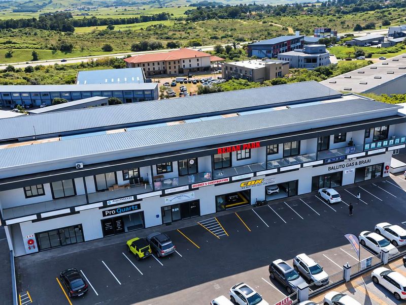 Aerial view of a modern multi-level commercial retail park featuring ground-floor storefronts, upper-level office spaces, and a paved parking area.
