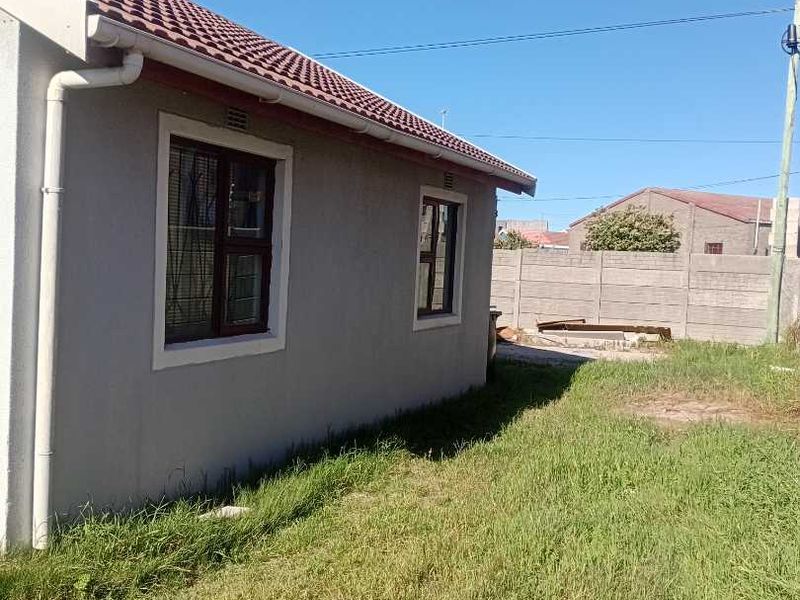 Rear view of the house featuring a tiled roof, guttering system, and a precast concrete boundary wall with an overgrown lawn area.