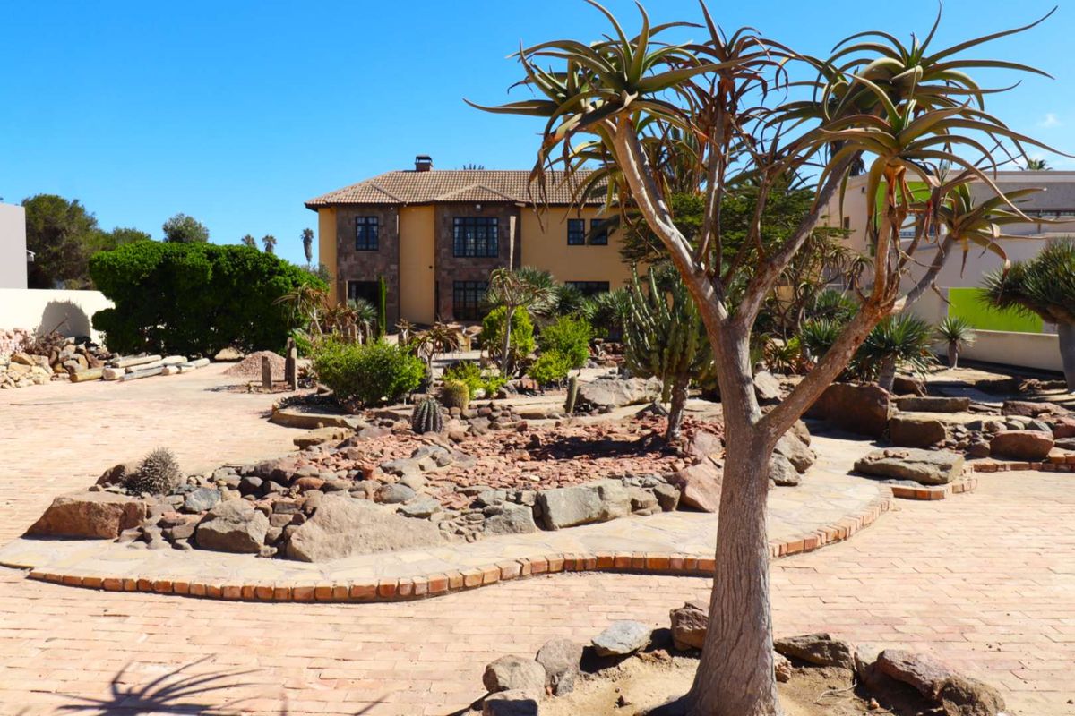 A spacious rear garden featuring a landscaped rockery, mature succulent plants, and brick-paved pathways leading to the two-story residential building.