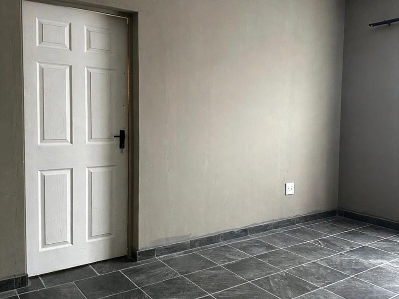 A clean, empty bedroom featuring neutral grey walls, dark slate-style floor tiles, and a white panel door.