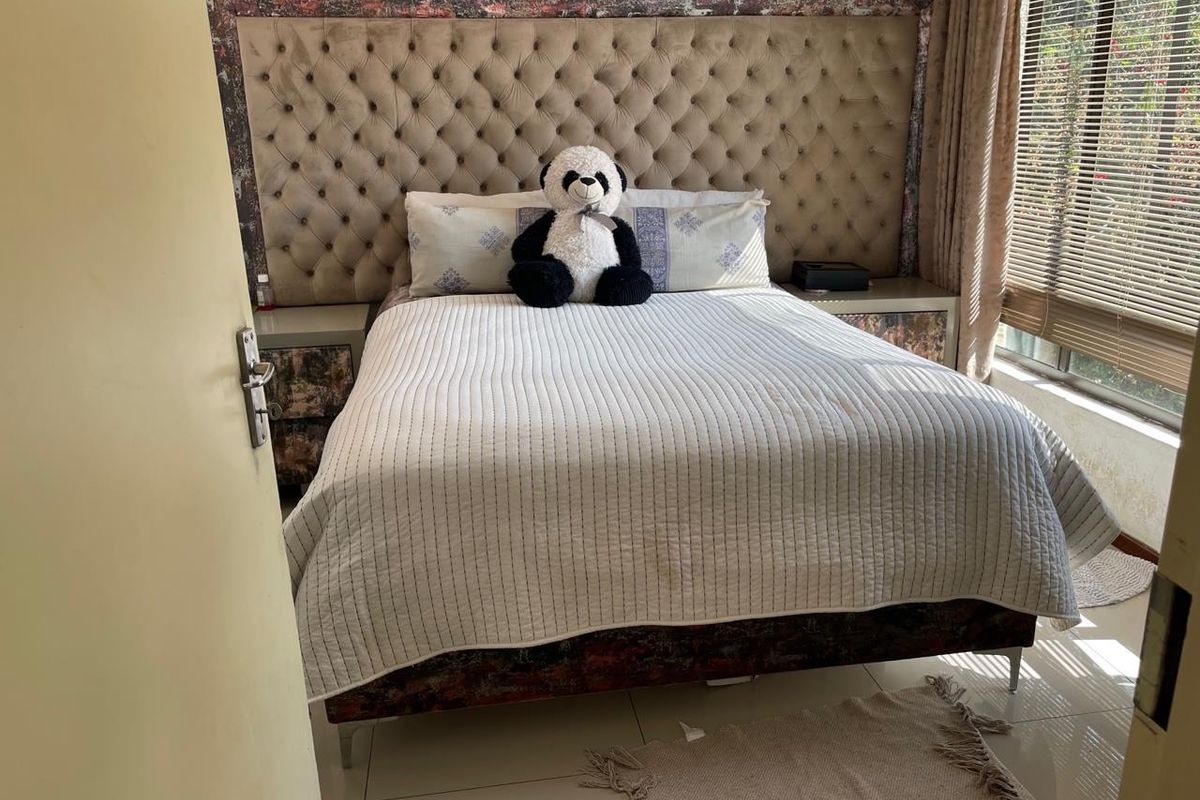 A bedroom featuring a large tufted headboard with integrated bedside tables, tiled flooring, and venetian blinds.