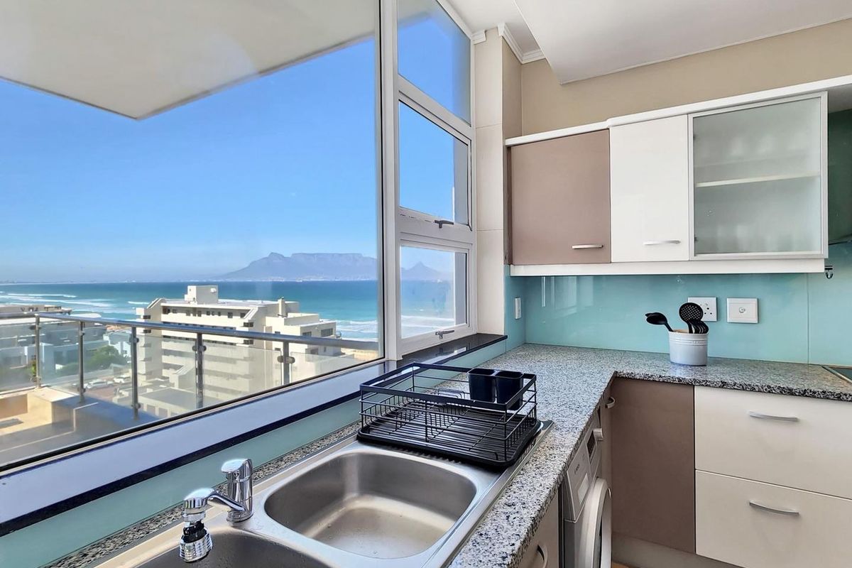 Modern kitchen featuring granite countertops, glass splashback, and built-in cabinetry, offering expansive ocean and mountain views through large windows.