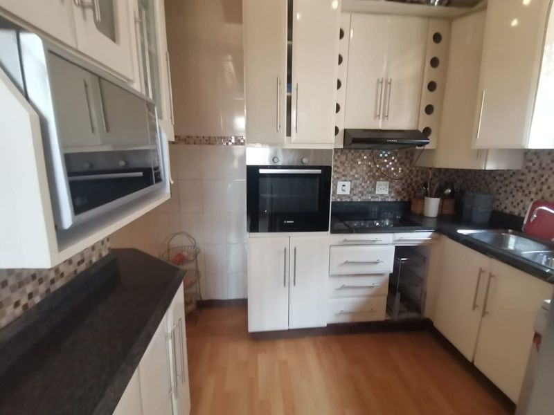 A functional kitchen featuring built-in appliances, dark countertops, tiled backsplash, and ample cabinetry, though one lower cabinet door is currently missing.