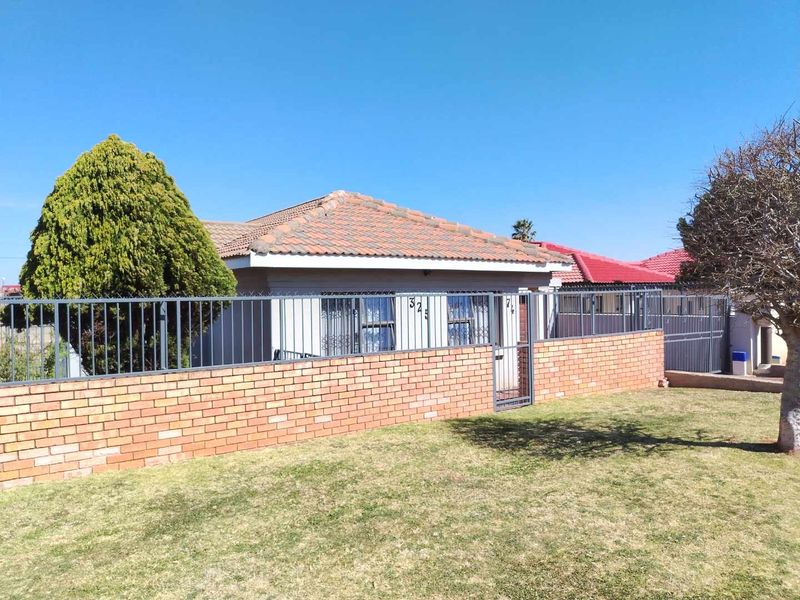 Front view of a residential house featuring a brick boundary wall, metal security fencing, and a tiled roof.