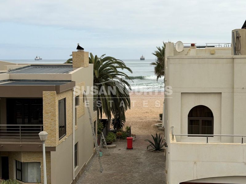 An elevated view looking down a paved driveway between two townhouse structures towards the beach and ocean.