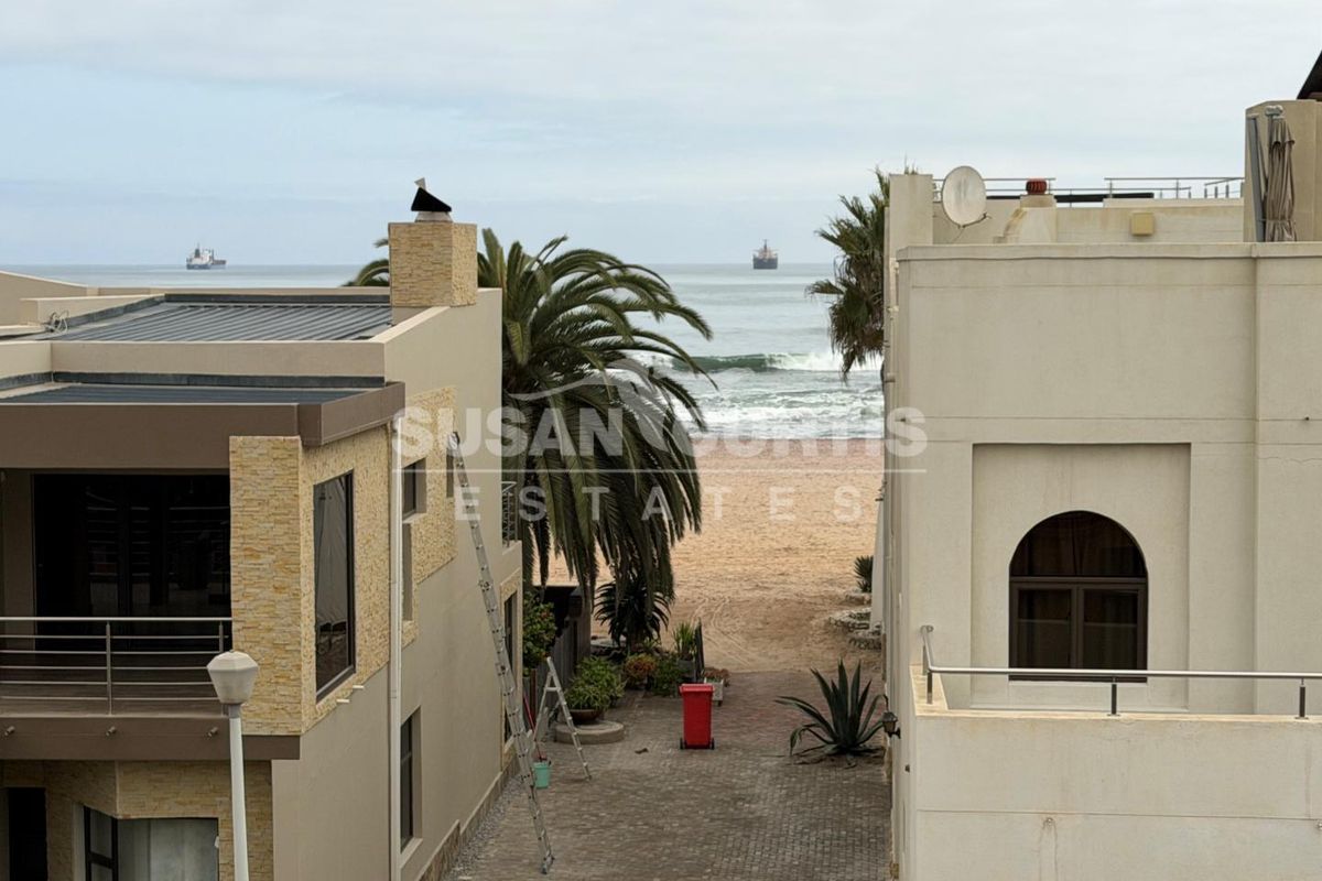 An elevated view looking down a paved driveway between two townhouse structures towards the beach and ocean.