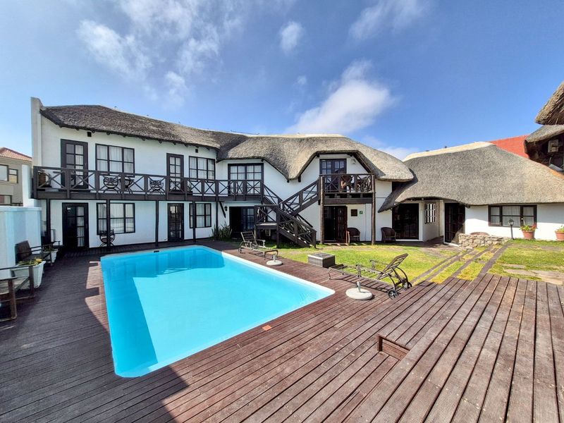 Spacious outdoor pool area featuring a swimming pool, extensive timber decking, and a two-story building with a traditional thatch roof and balcony access.