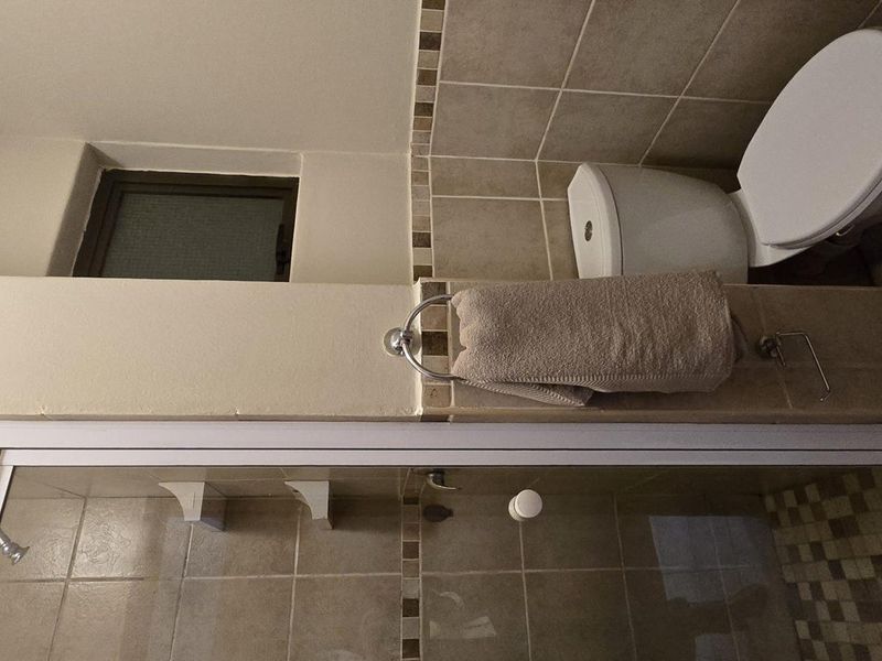 A functional bathroom featuring a shower enclosure with tiled walls and flooring, complemented by a standard toilet and window.