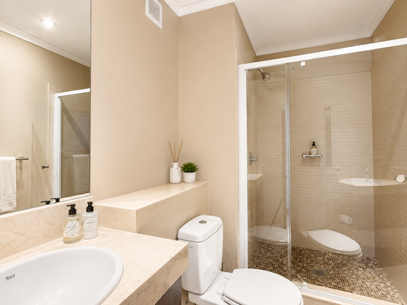 A well-maintained bathroom featuring a vanity basin, toilet, and a glass-enclosed shower with mosaic tile flooring and neutral wall finishes.