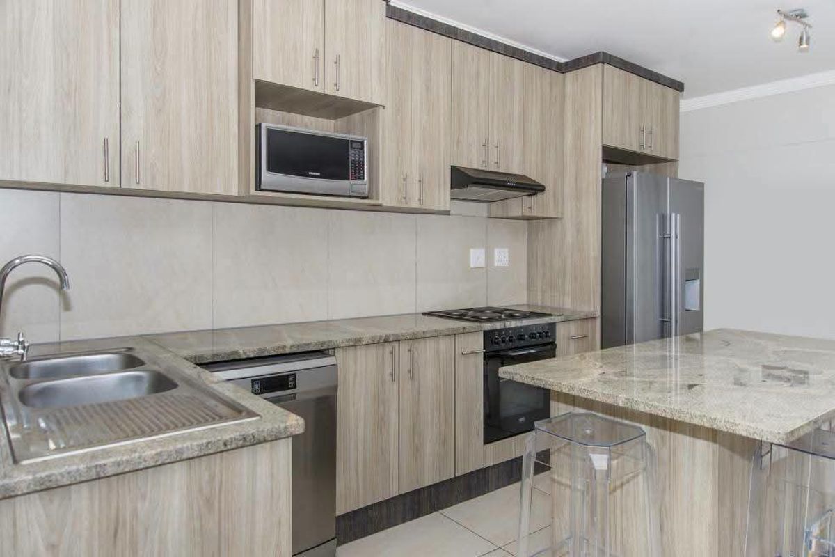 Modern kitchen featuring light wood-grain cabinetry, granite countertops, a central island, and integrated appliances including a gas hob and built-in oven.