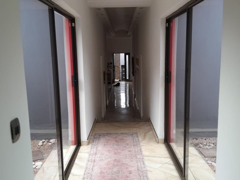 A bright, tiled hallway featuring large sliding glass doors on both sides, providing natural light and access to external areas.