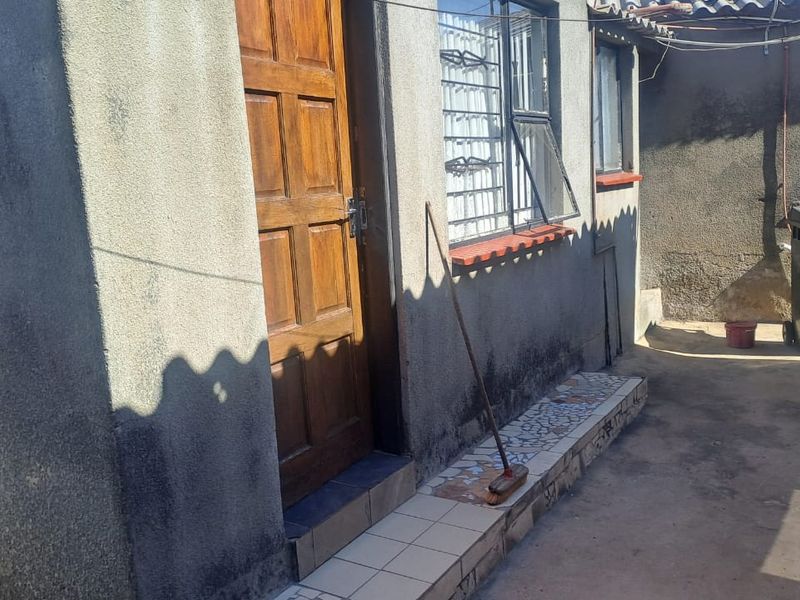 Rear exterior view of the property featuring a wooden door, security bars on windows, and a tiled step area with plastered wall finish.