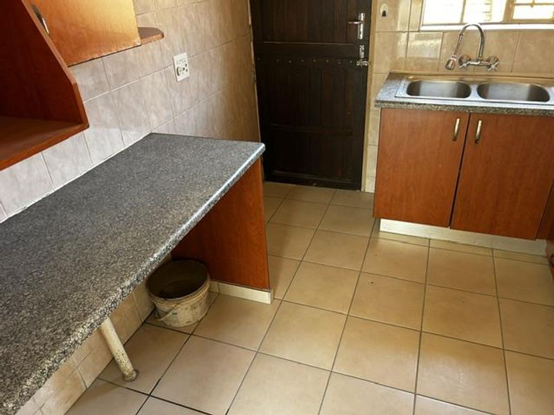 A functional kitchen area featuring laminate cabinetry, a double stainless steel sink, and tiled surfaces, offering a practical layout ready for modernization.