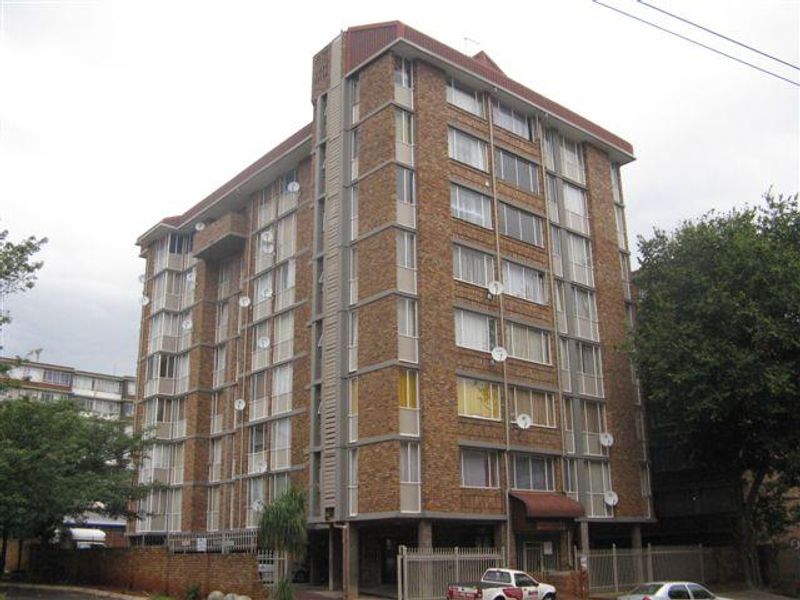 A multi-story brick apartment building featuring a secure perimeter fence and multiple satellite dish installations on the facade.