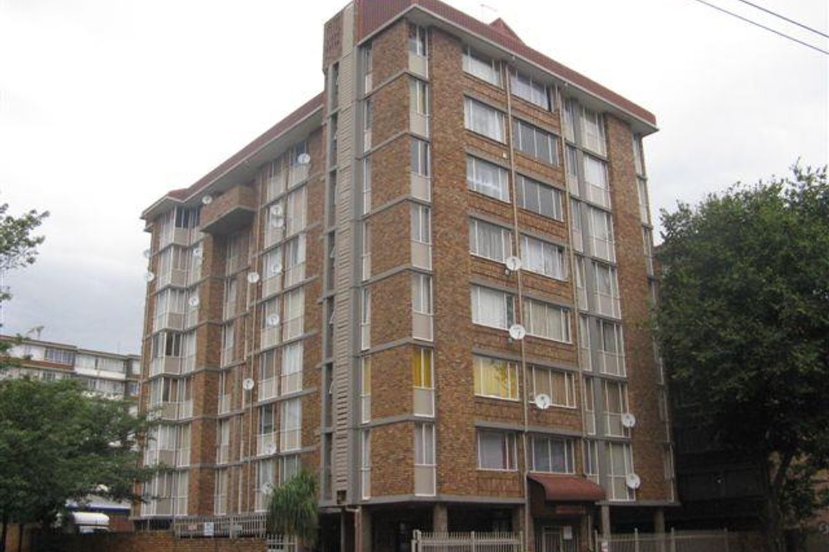 A multi-story brick apartment building featuring a secure perimeter fence and multiple satellite dish installations on the facade.