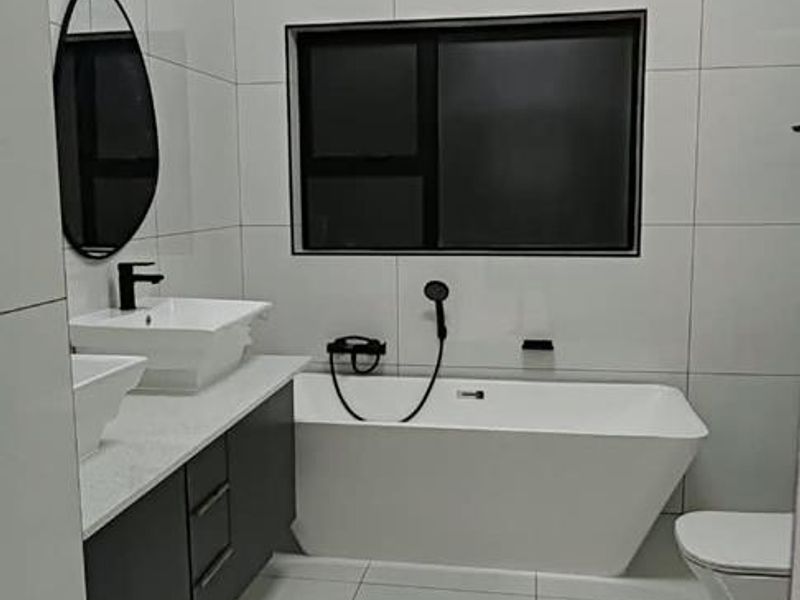 Modern bathroom featuring a sleek freestanding bathtub, double vanity with vessel sinks, and contemporary floor-to-ceiling tiling.