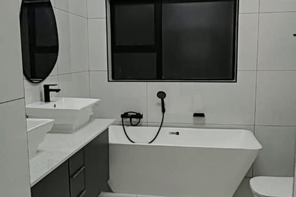Modern bathroom featuring a sleek freestanding bathtub, double vanity with vessel sinks, and contemporary floor-to-ceiling tiling.