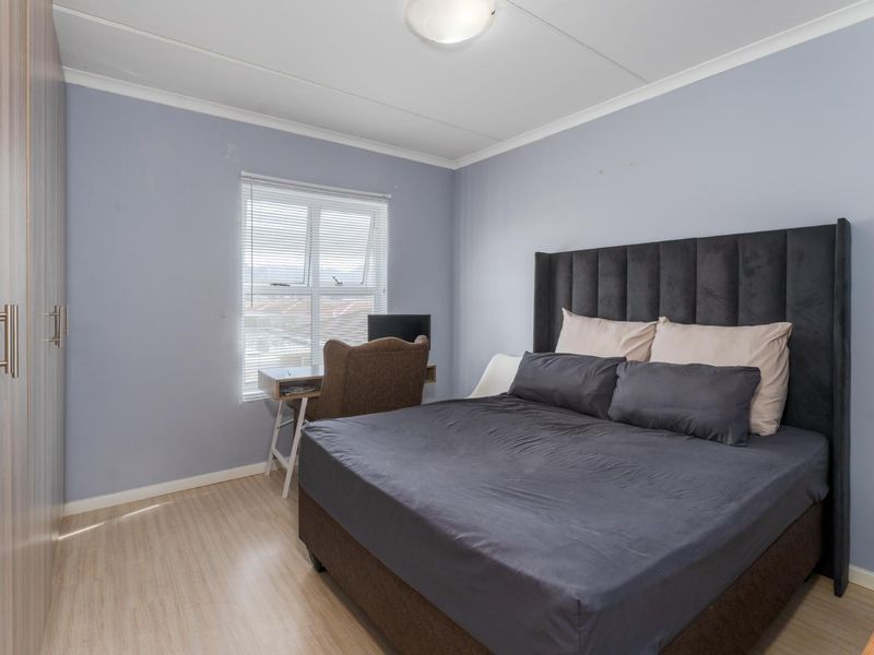 A well-lit bedroom featuring laminate flooring, built-in cupboards, and venetian blinds, providing a functional and comfortable living space.