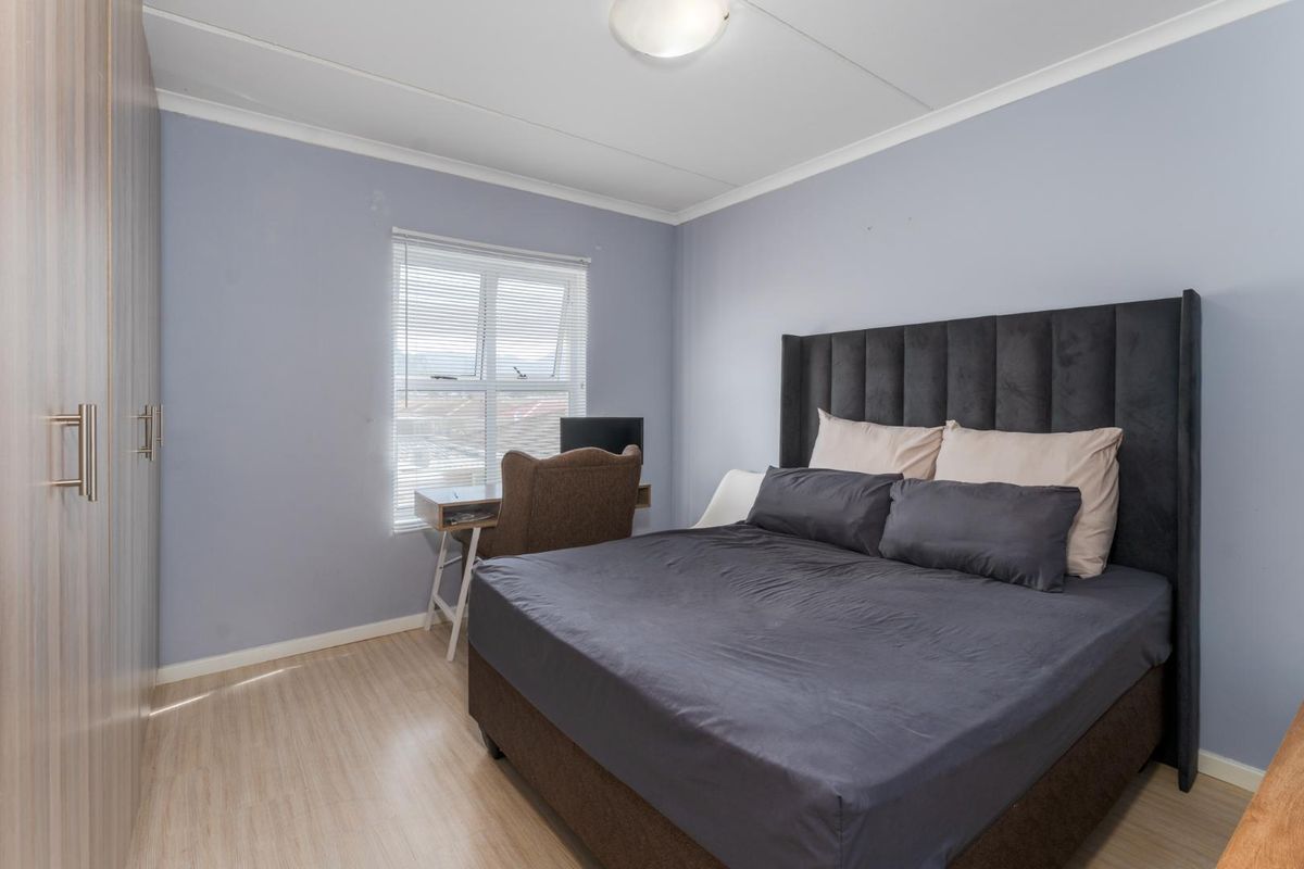 A well-lit bedroom featuring laminate flooring, built-in cupboards, and venetian blinds, providing a functional and comfortable living space.