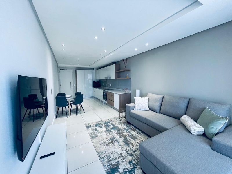 Modern open-plan living area featuring a sleek kitchen with built-in appliances, stone countertops, and polished tiled flooring throughout.