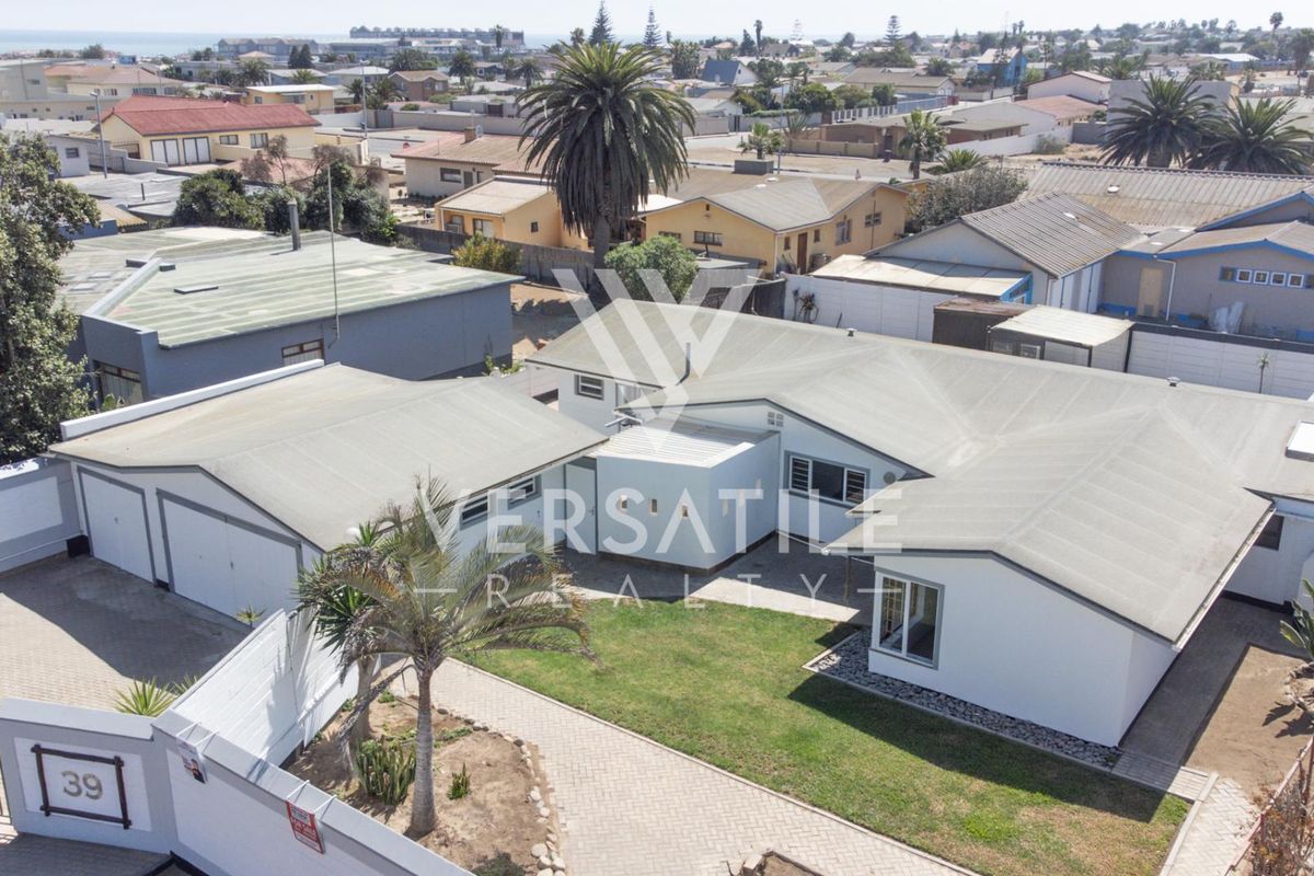 Aerial view of the property showing the main house, garage, paved driveway, and surrounding garden area within a residential neighborhood.